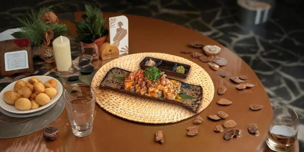 Plated gourmet dish served on a decorative tray at a restaurant table, surrounded by bread rolls, dipping sauces, candles, greenery, and table decor in a warm indoor setting.