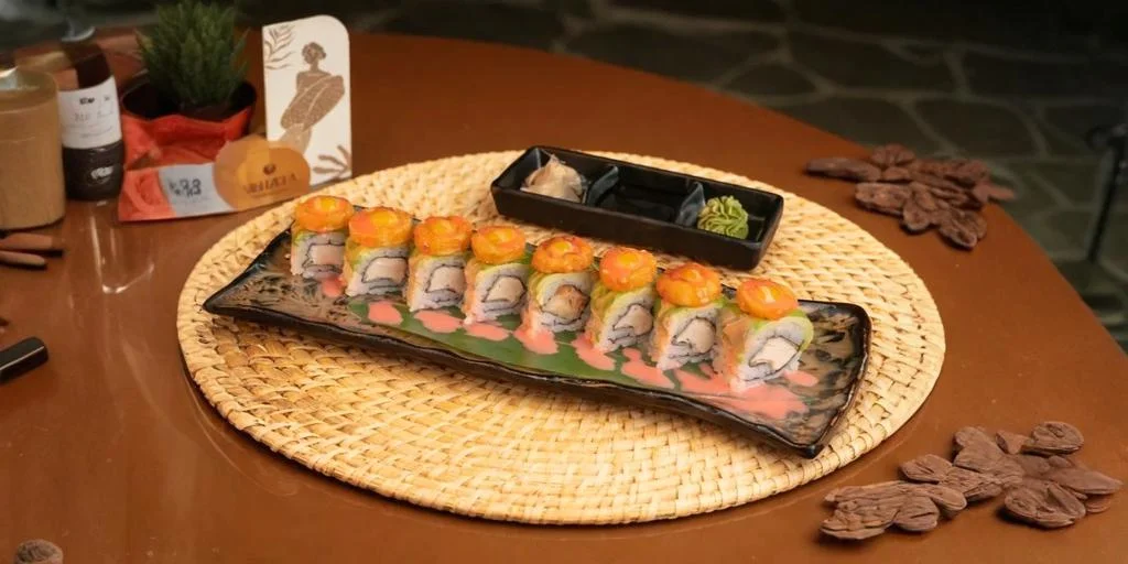 Sushi rolls neatly arranged on a rectangular plate with dipping sauces, served on a woven placemat on a wooden dining table.